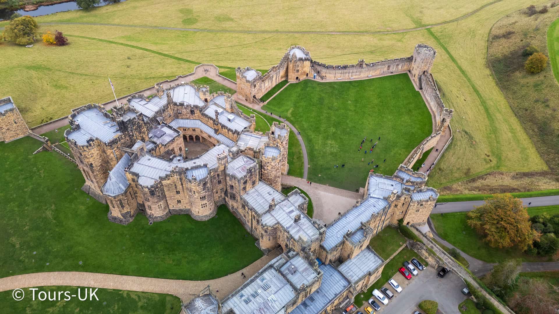 Drone aerial view of Alnwick Castle and the town of Alnwick, Northumberland, England, surrounded by lush countryside and historic stone architecture.