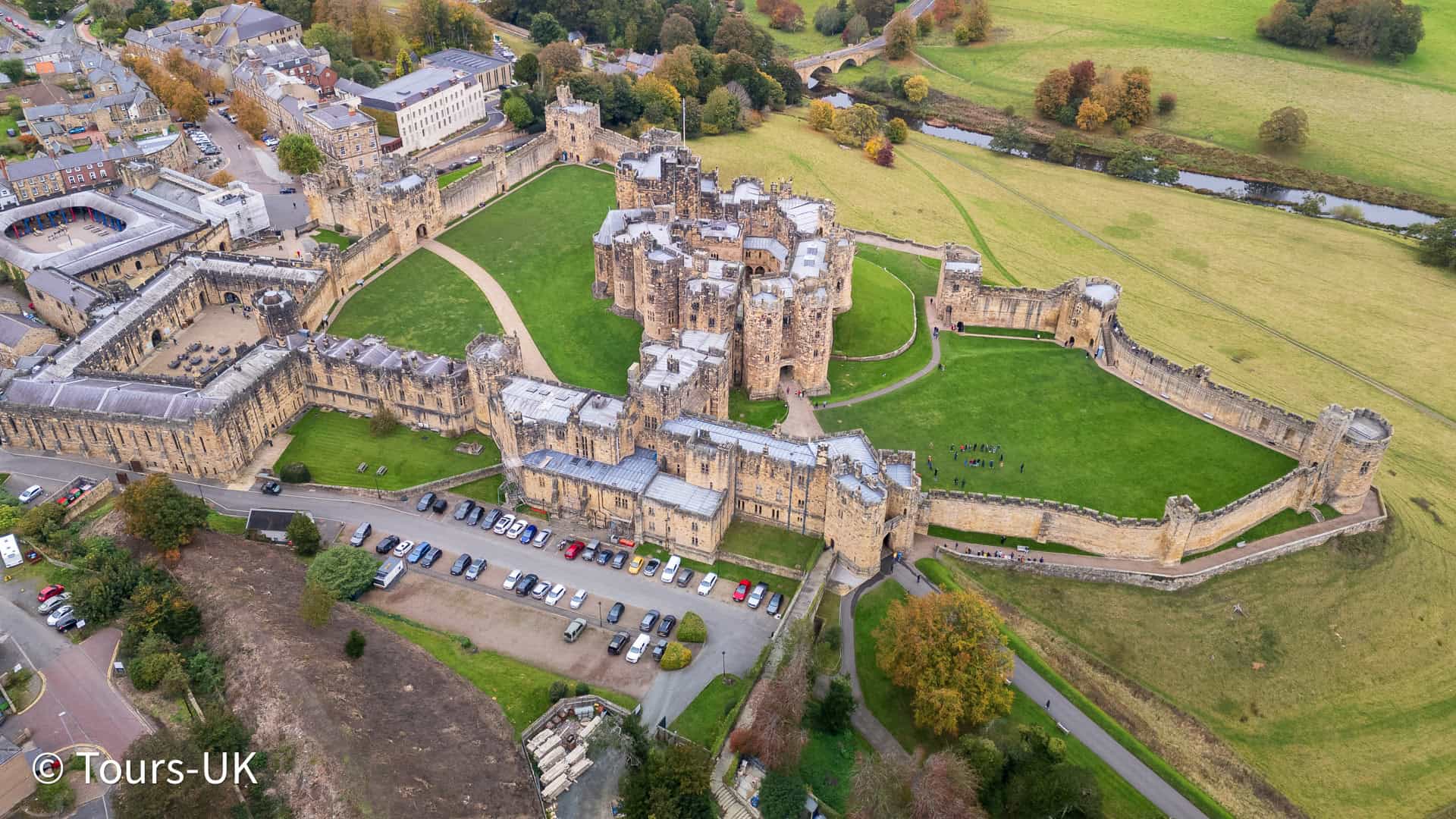 Drone aerial view of Alnwick Castle and the town of Alnwick, Northumberland, England, surrounded by lush countryside and historic stone architecture.