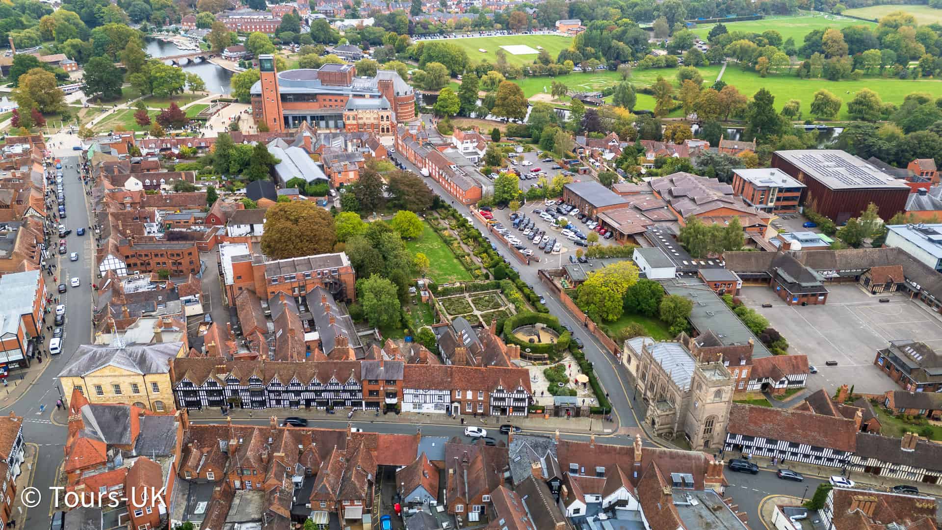 Aerial drone view of Stratford-upon-Avon town centre with Tudor-style buildings, cobbled streets, and the River Avon winding through the historic landscape.