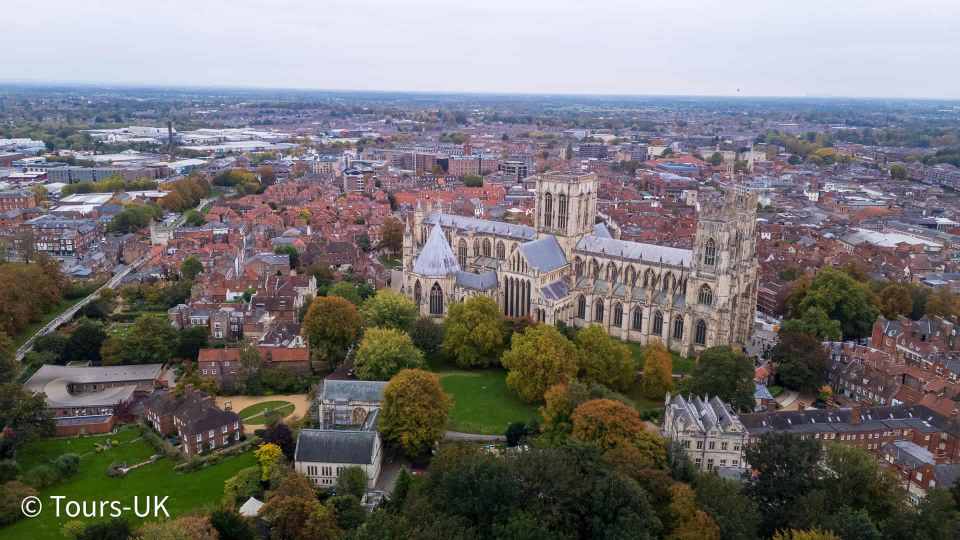Aerial view of York Cathedral surrounded by historic buildings and colourful autumn trees in the city centre.